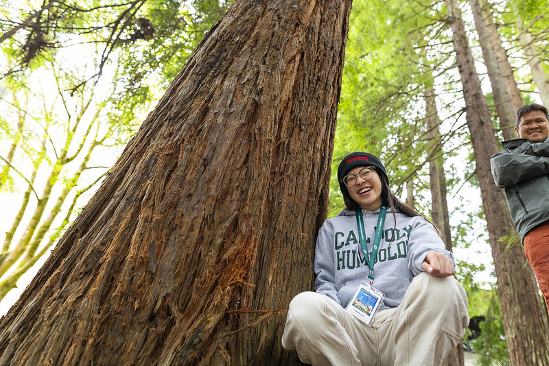 cal poly humboldt student smiles while sitting under tree