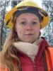 Sylvia Royen in the forest wearing a yellow hard hat, a beige scarf, red coat and an orange vest.